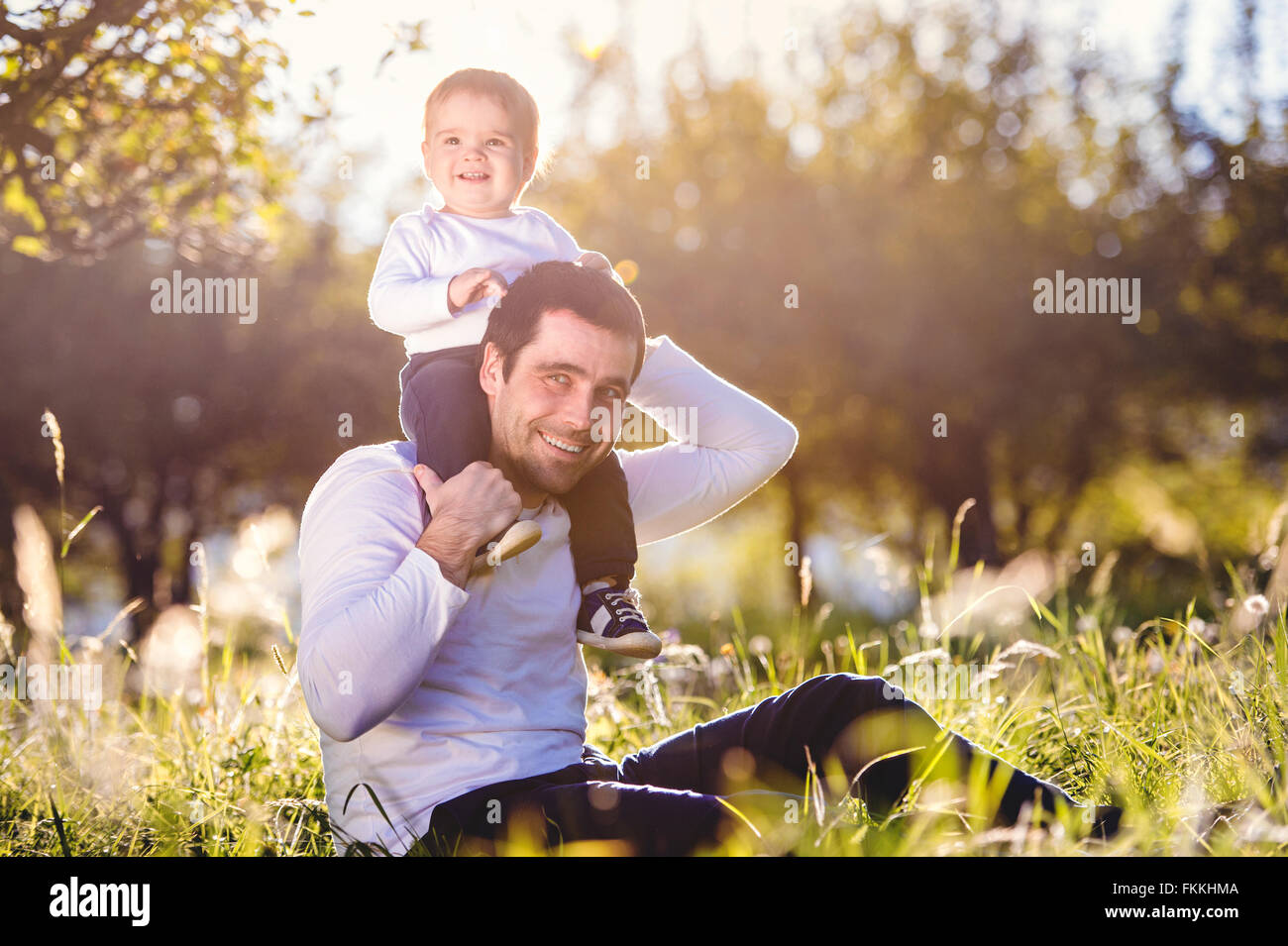 Father carrying son on shoulders, sitting on the grass Stock Photo