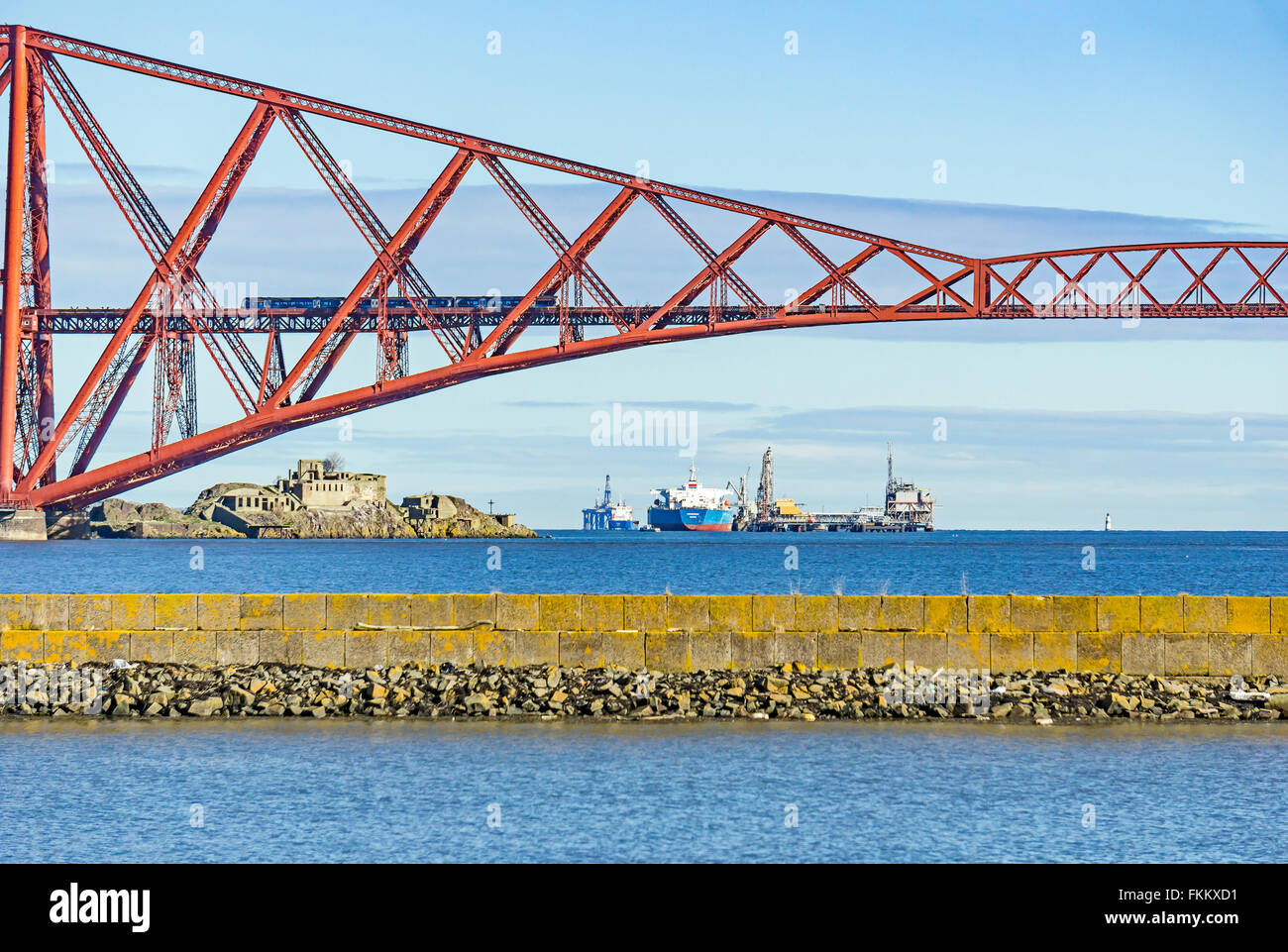 Train passing the Forth Bridge across Firth of Forth at South Queensferry with tanker at Hound Point and Inchgarvie island left. Stock Photo