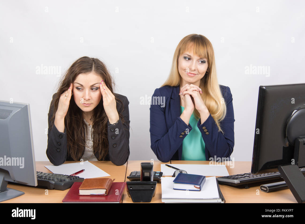 The situation in the office - girl happily looking at a computer screen, the other a girl with a headache looking at the screen Stock Photo