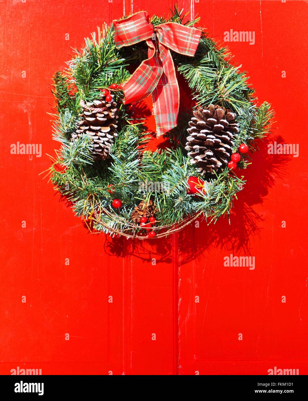 Christmas holiday pine wreath with pinecones and red bow on a red door ...