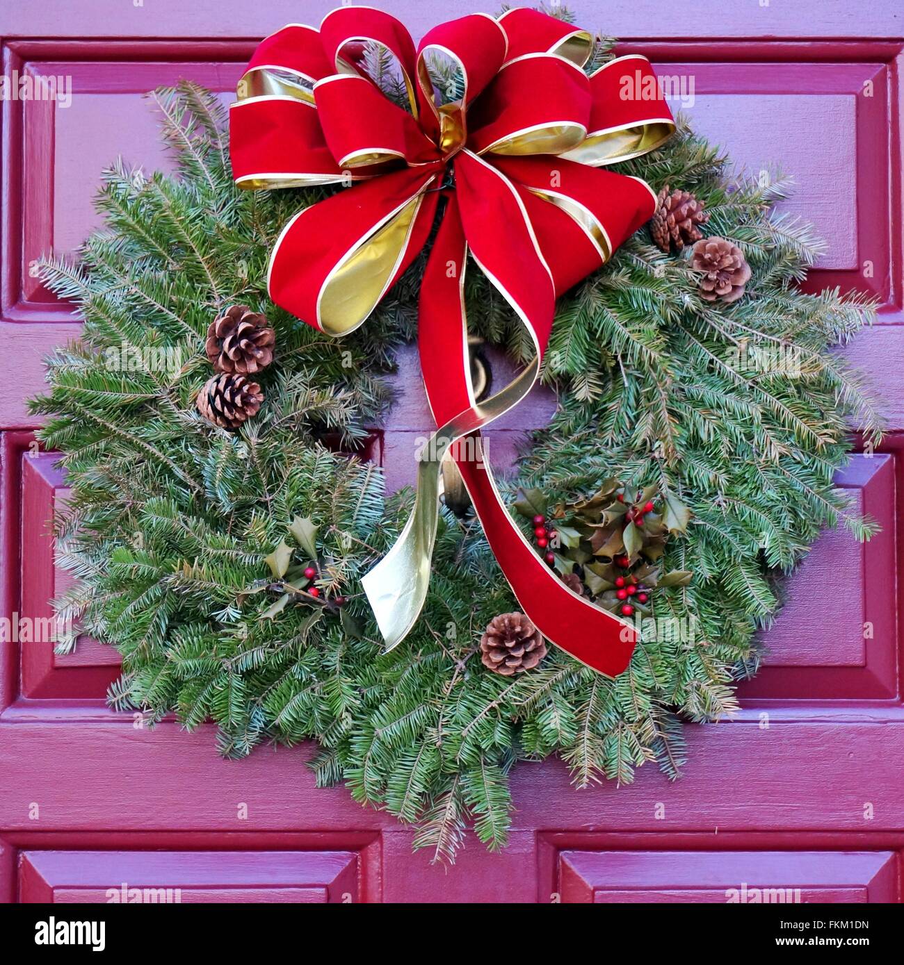 Christmas holiday pine wreath with pinecones and red bow on a red door ...