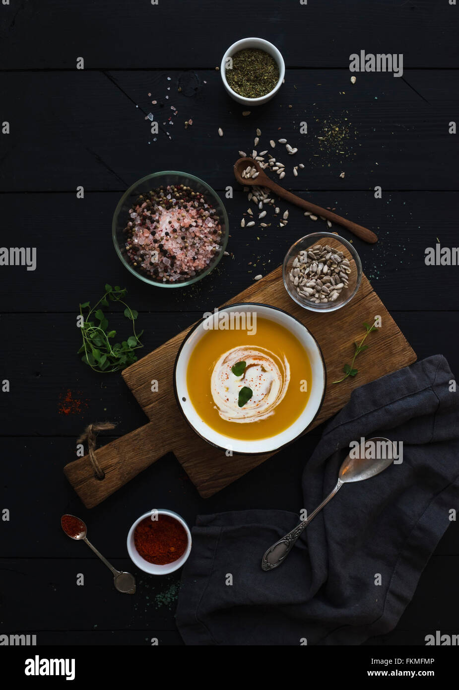 Pumpkin soup with cream, seeds and spices in rustic metal bowl on wooden board over grunge black background. Top view Stock Photo