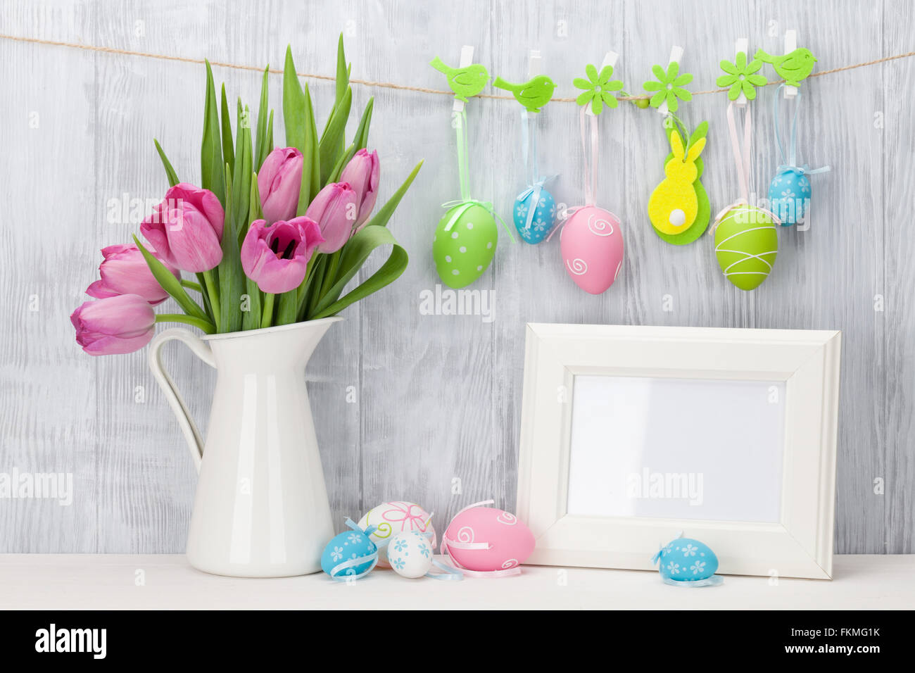 Easter eggs, blank photo frame and pink tulips bouquet on shelf in ...