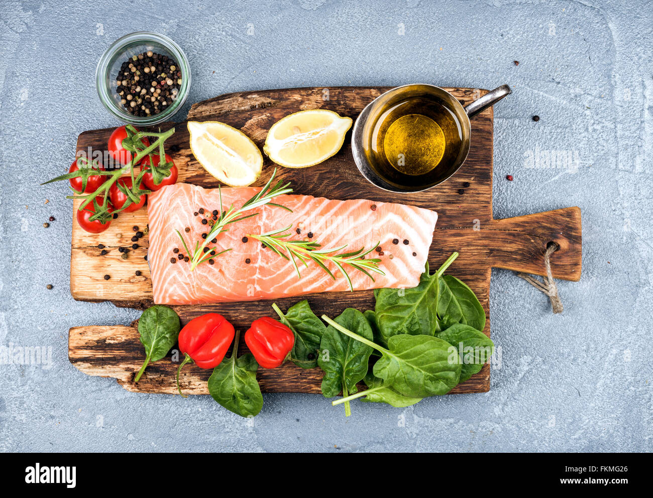 Ingredients for cooking healthy dinner. Raw salmon fillet, spinach, tomatoes, olive oil, lemon, peppers, rosemary and spices on Stock Photo