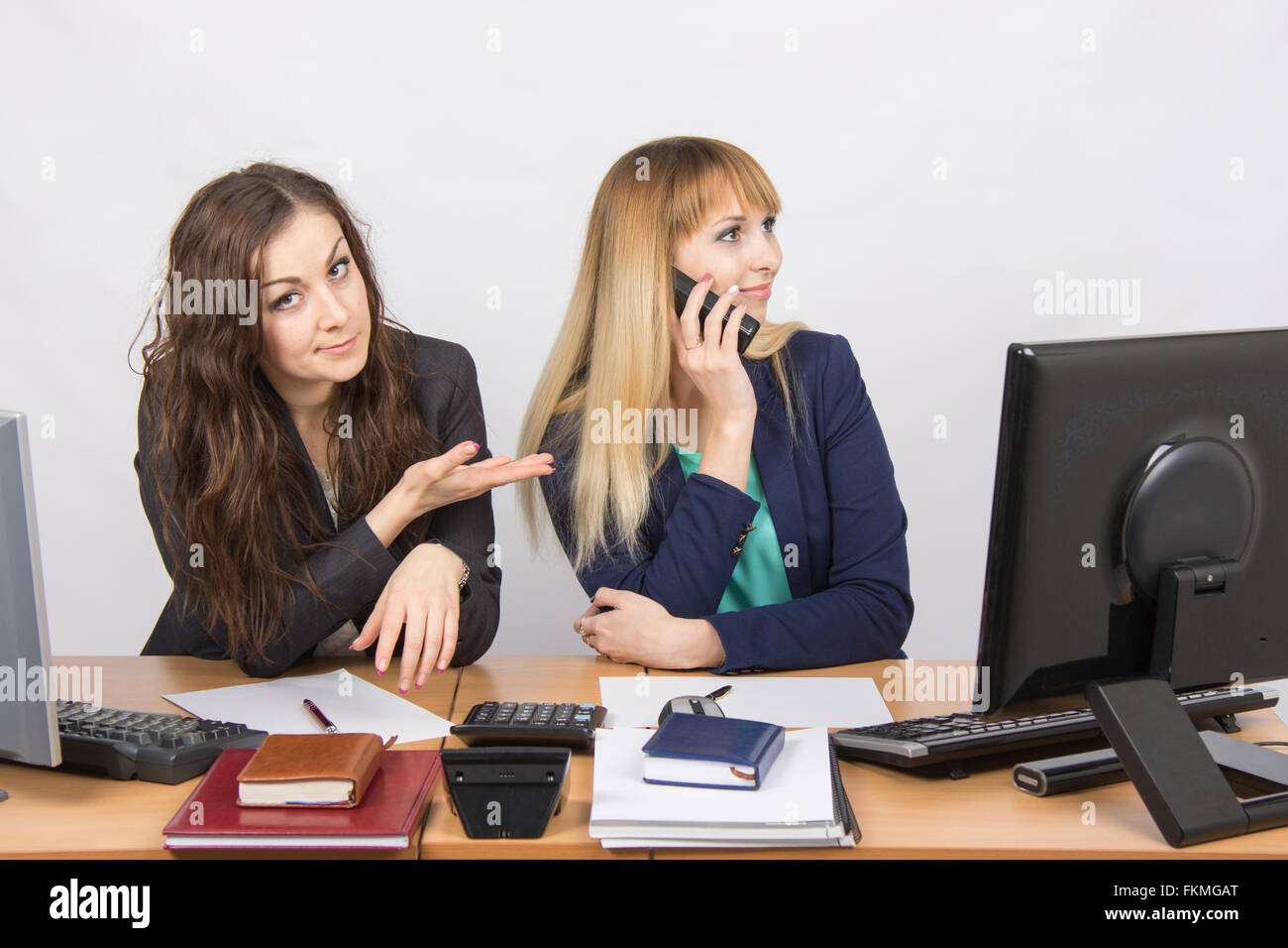 The situation in the office - one employee on the phone, the other asks for her phone Stock Photo
