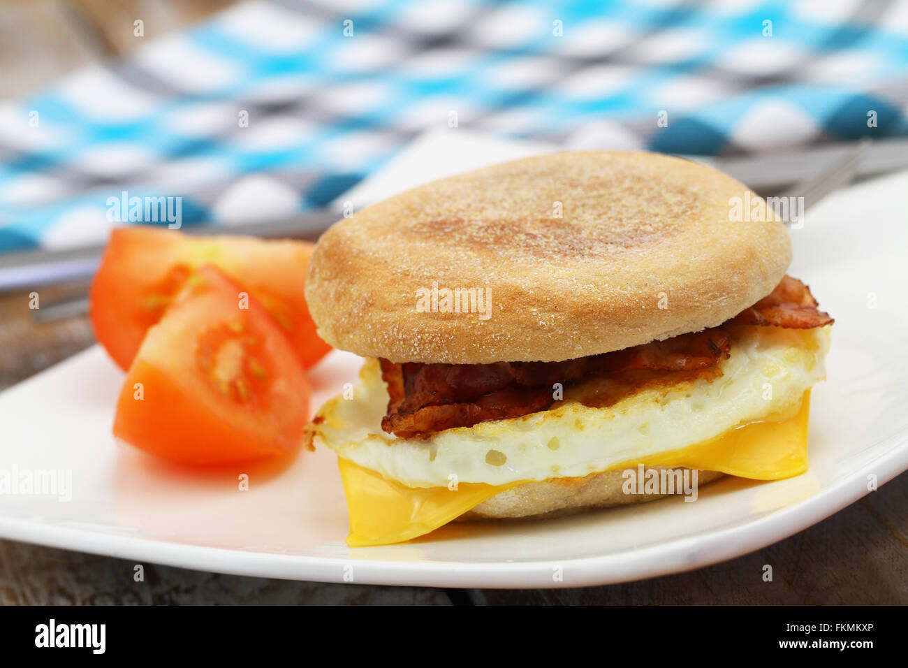 Egg and bacon muffin on white plate with slices of tomato on the side Stock Photo