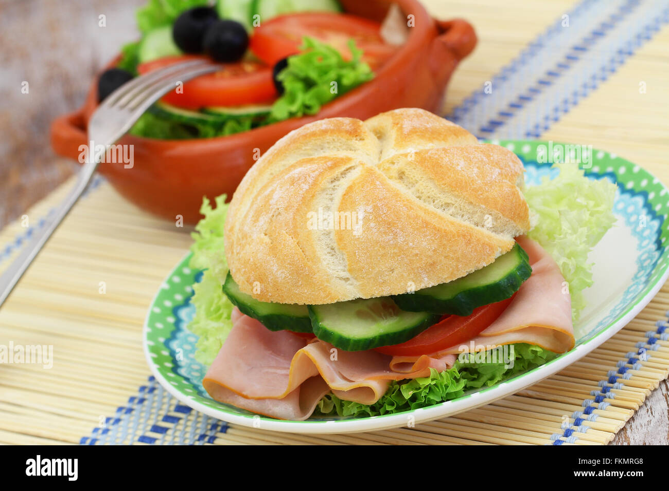 Lunch consisting of ham roll with lettuce, tomato and cucumber and bowl