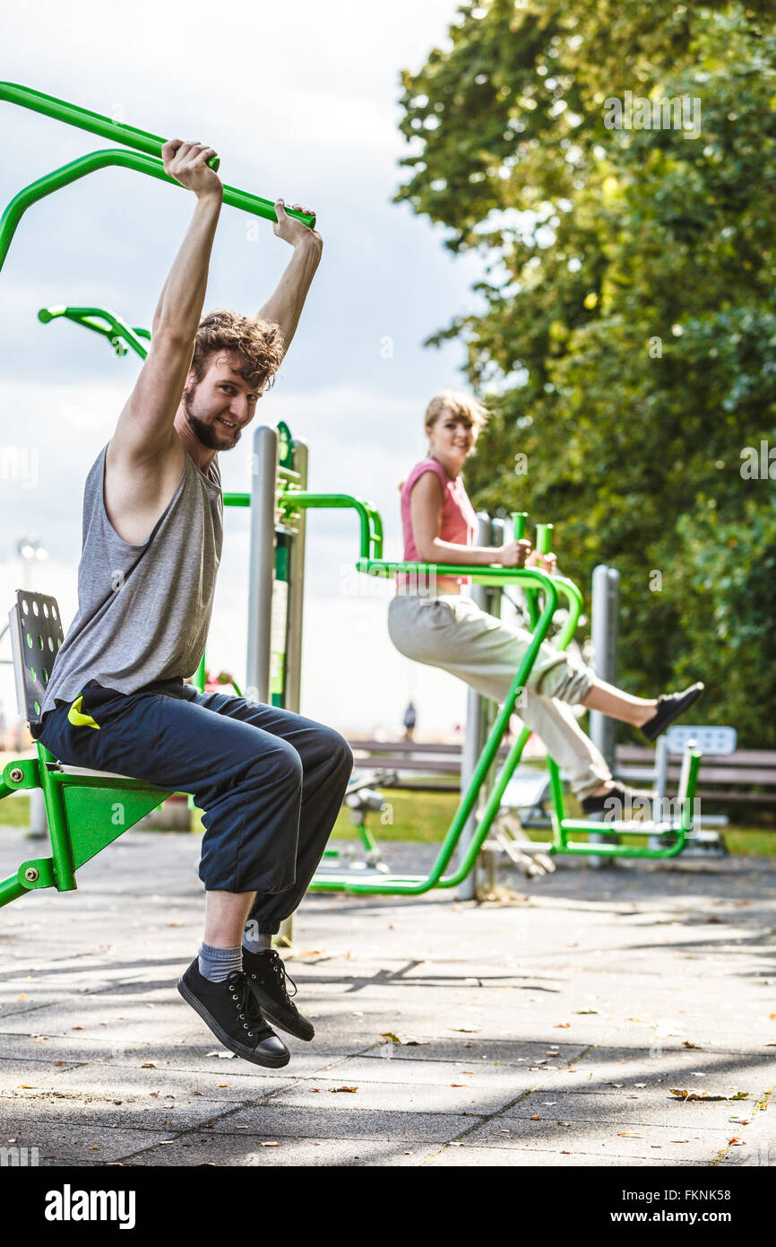 Active young man exercising on chest press machine and woman on leg raise. Muscular strong guy and girl in training suit working out at outdoor gym. Sport fitness and healthy lifestyle concept
