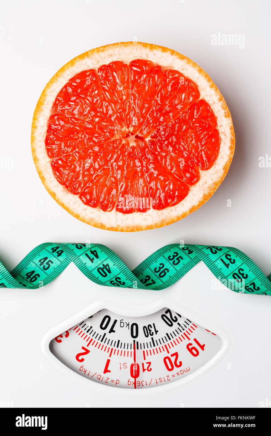 Dieting healthy eating slim down concept. Closeup grapefruit slice with measuring tape on white weight scale Stock Photo