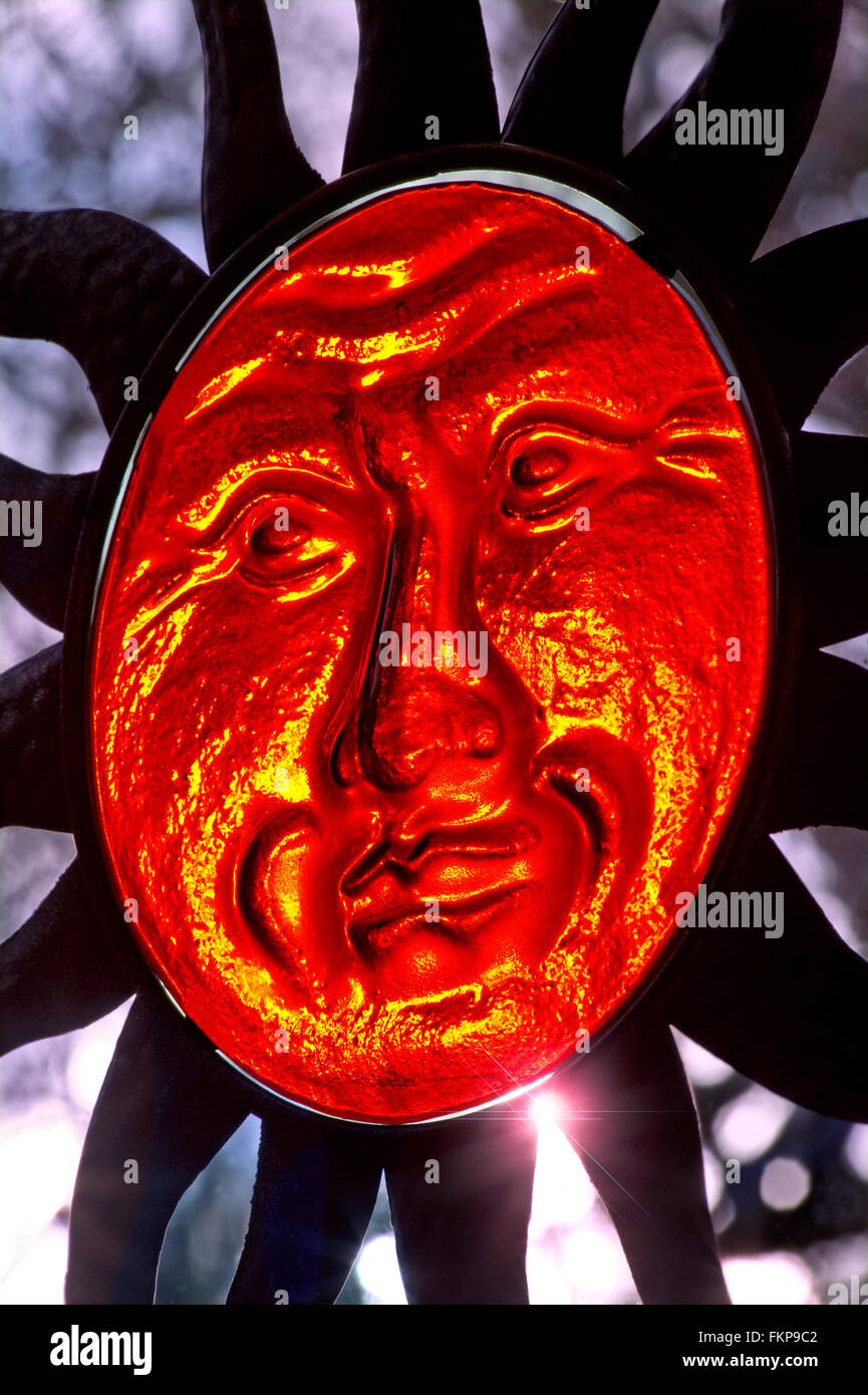 Translucent glass face of Sun God sculpture and extending rays with low setting sun illuminating its features Stock Photo