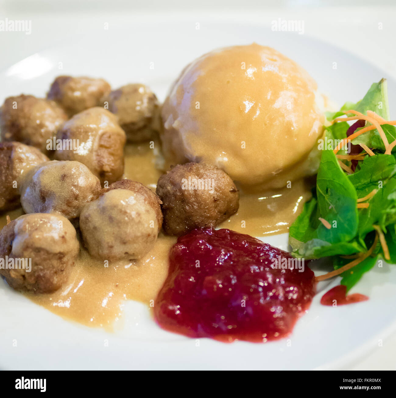 A plate of IKEA meatballs, mashed potatoes, cream gravy, green salad and lingonberry sauce. Stock Photo