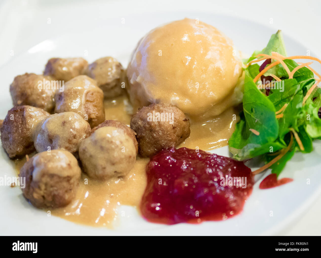 A plate of IKEA meatballs, mashed potatoes, cream gravy, green salad and lingonberry sauce. Stock Photo