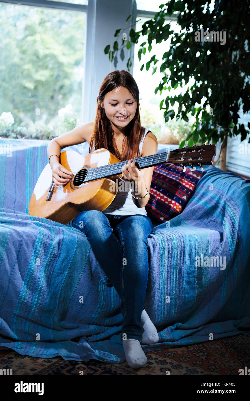 Mixed race woman playing guitar on sofa Stock Photo