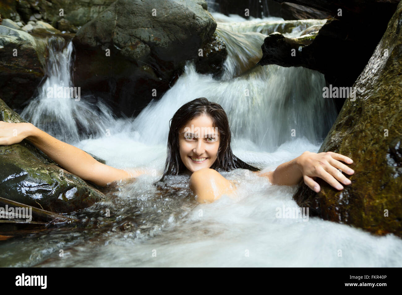 Mixed race woman sitting in waterfall Stock Photo