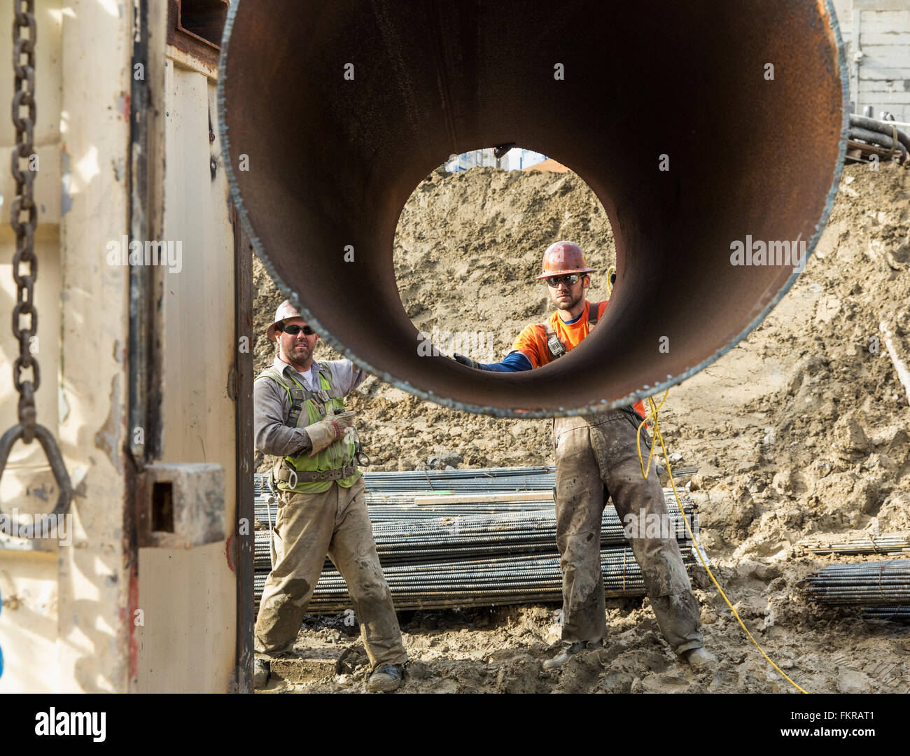 Caucasian workers hauling pipe at construction site Stock Photo