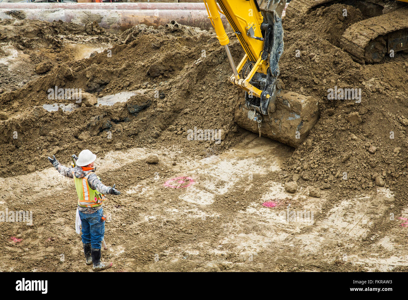 Caucasian worker directing digger at construction site Stock Photo