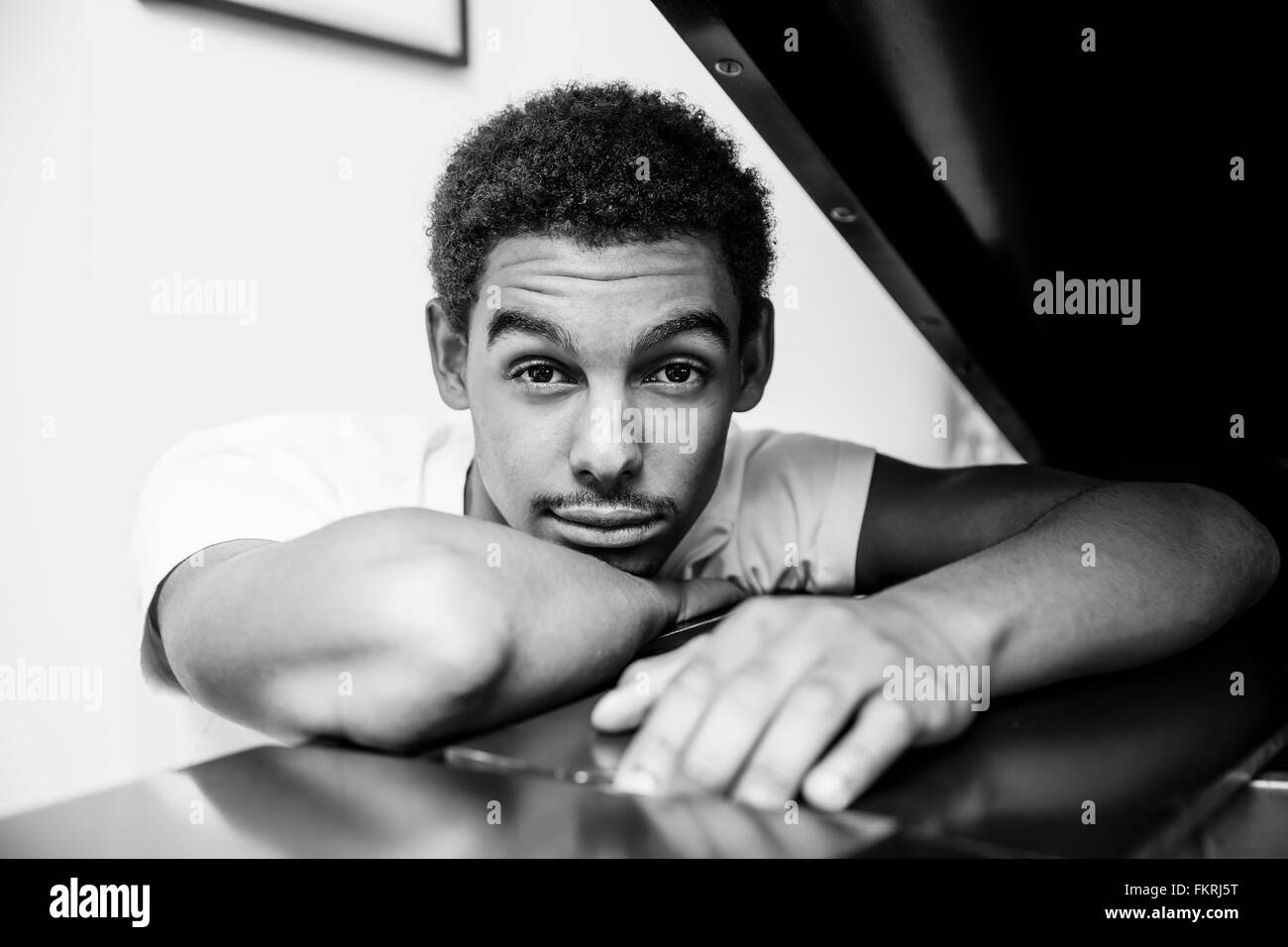 Mixed race man leaning on piano Stock Photo