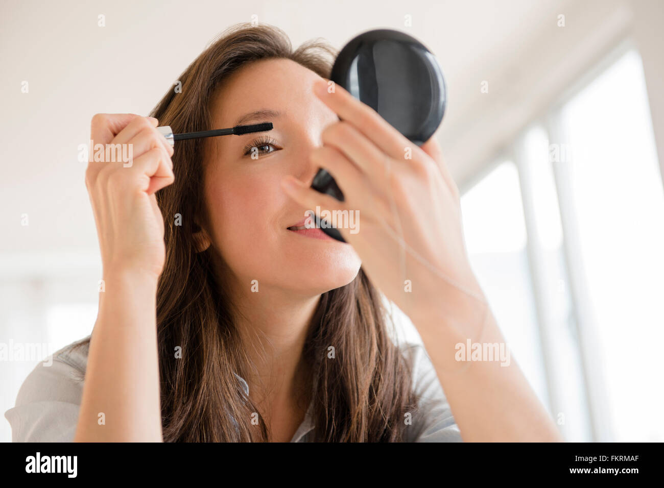 Mixed race woman applying makeup in compact mirror Stock Photo