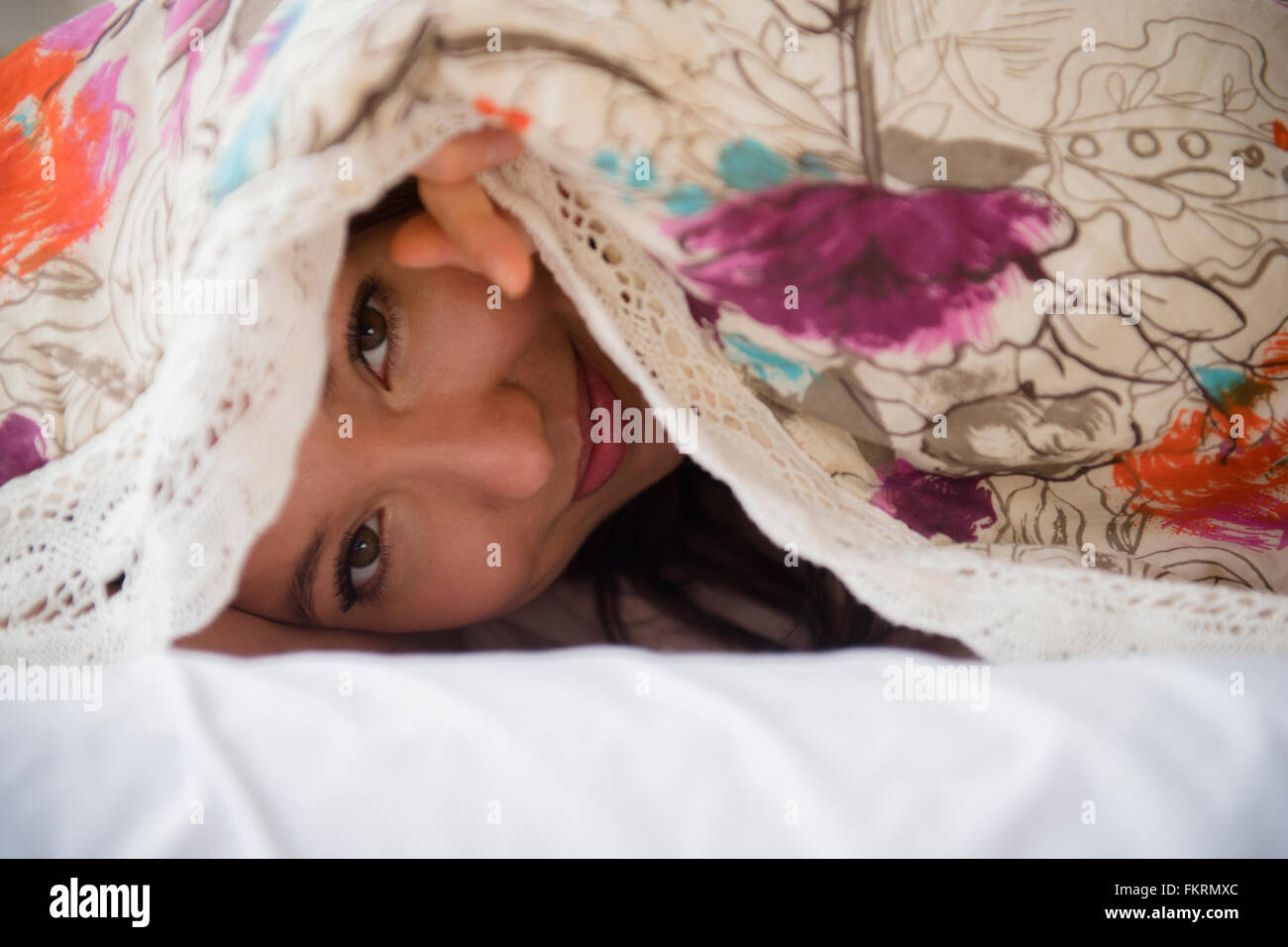 Mixed race woman peeking out from blanket Stock Photo