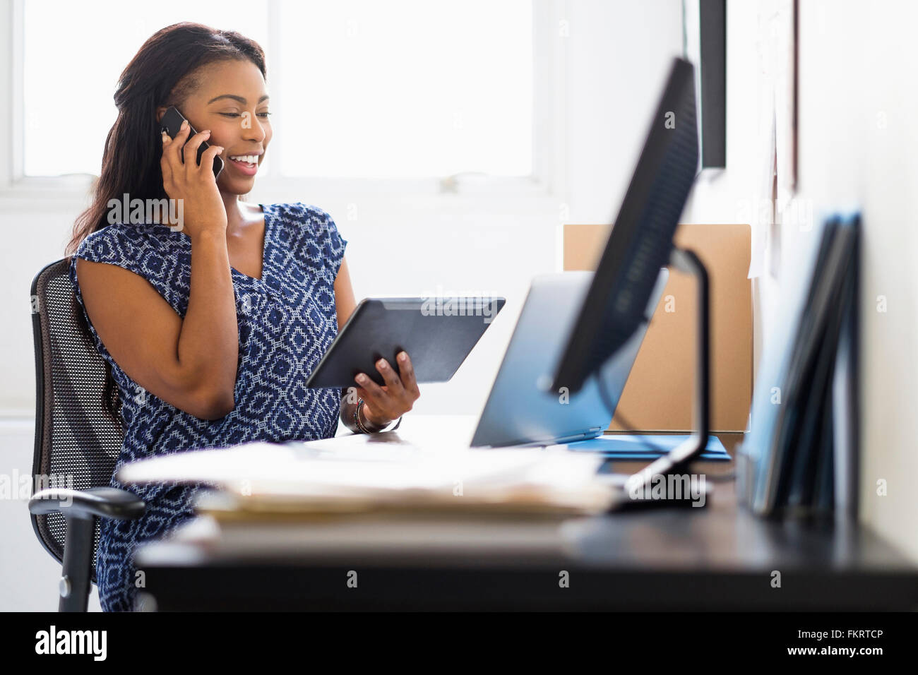 Mixed race woman multitasking in office Stock Photo