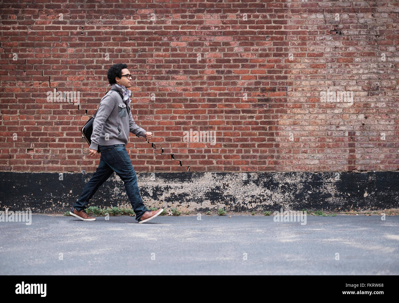 Mixed race man walking near brick wall Stock Photo