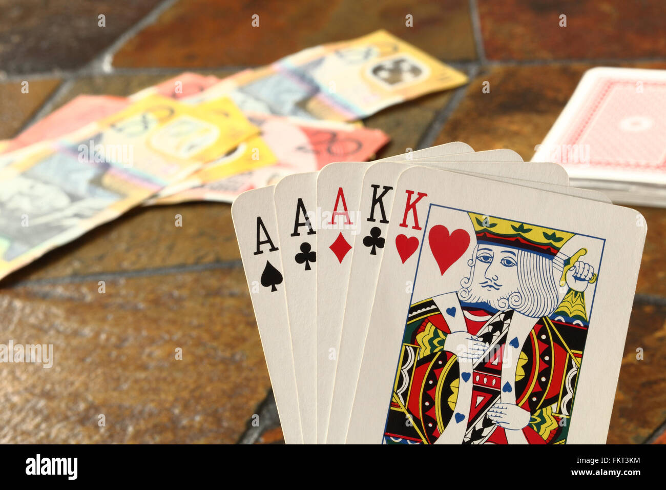 A 'Full House'  hand of cards in the foreground with Australian banknotes laying on a tiled table top Stock Photo