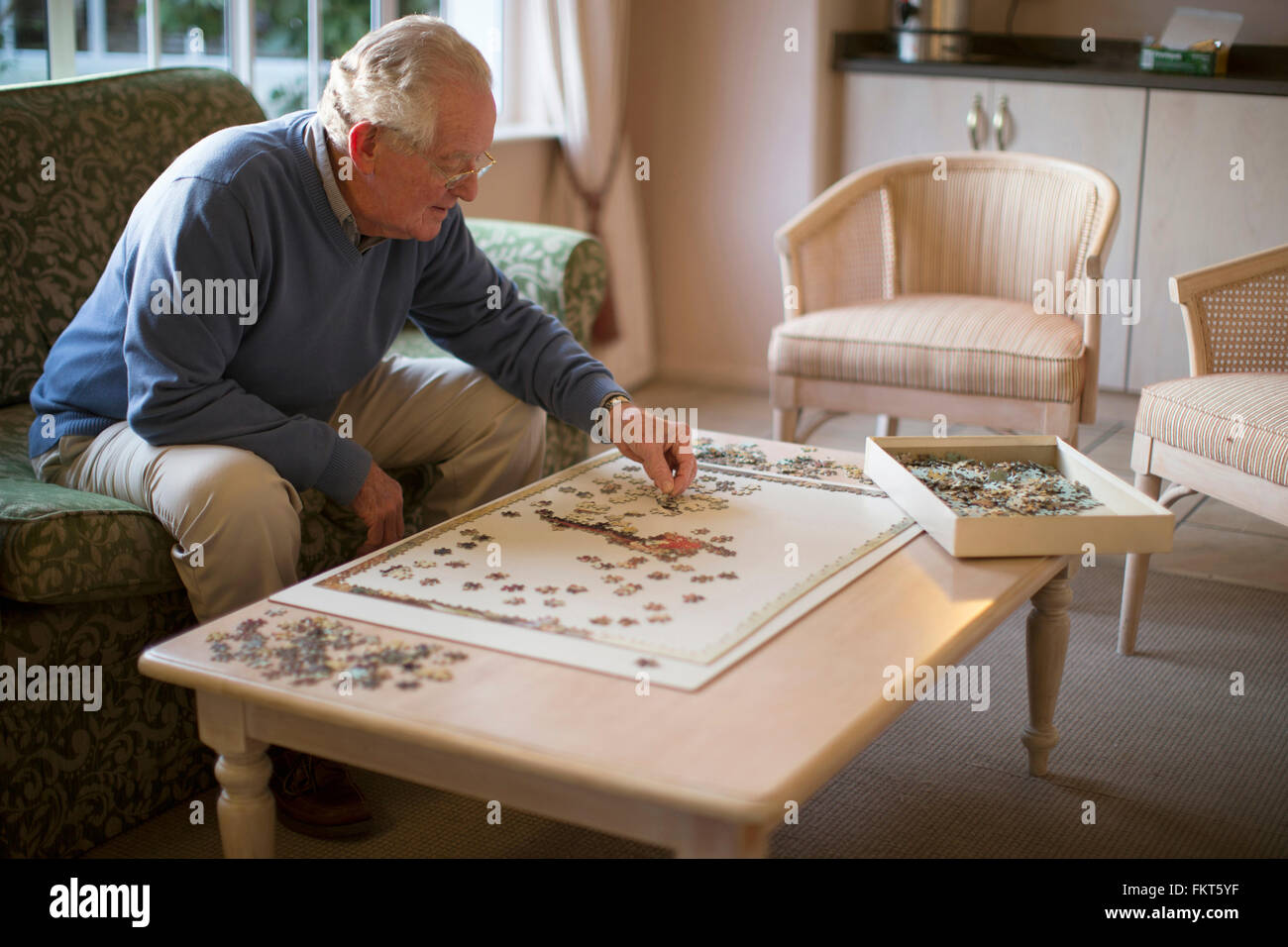 Older man on sofa solving jigsaw puzzle Stock Photo