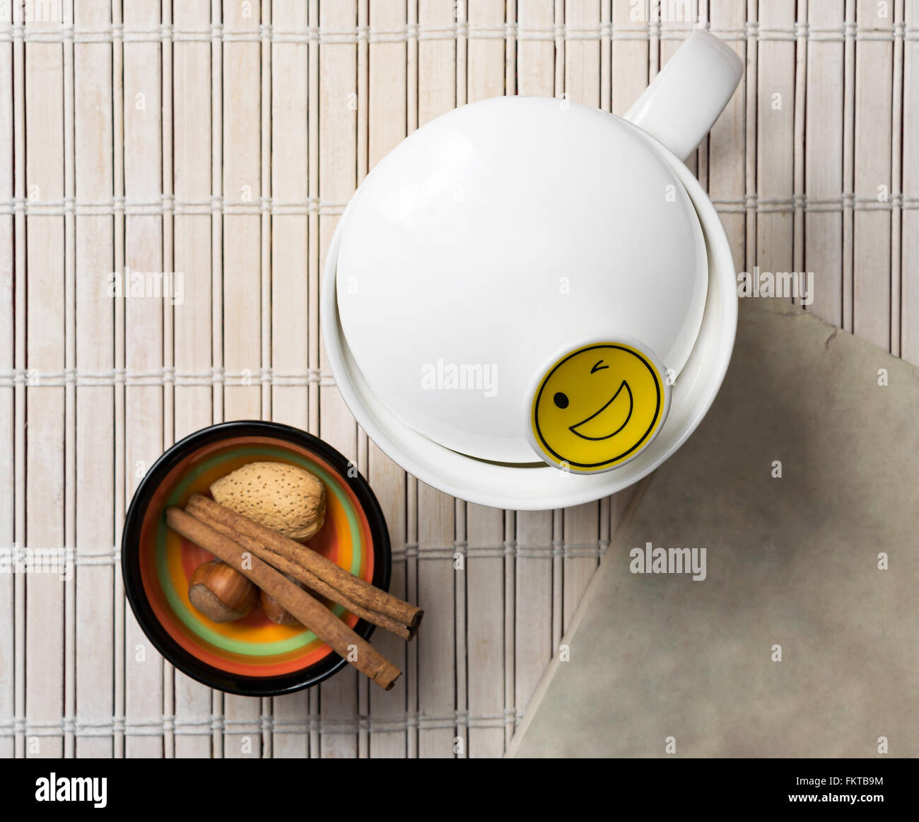 White mug with a smiley face emoji and Cinnamon sticks, nuts, and almond in a small colorful bowl Stock Photo