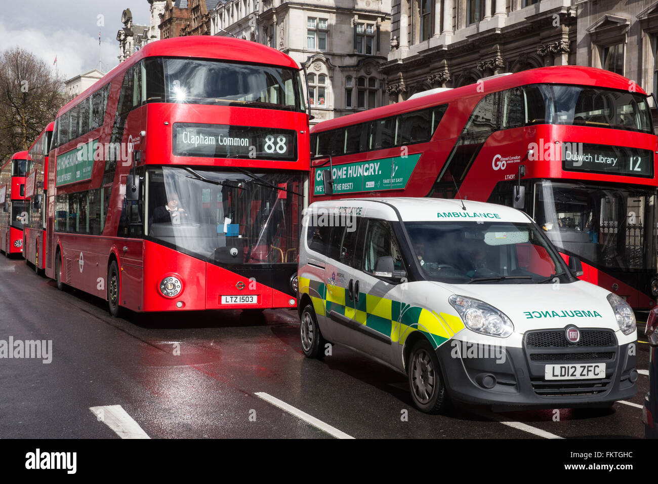 Iconic Red London buses in Whitehall near Parliament with an ambulance in the foreground Stock Photo