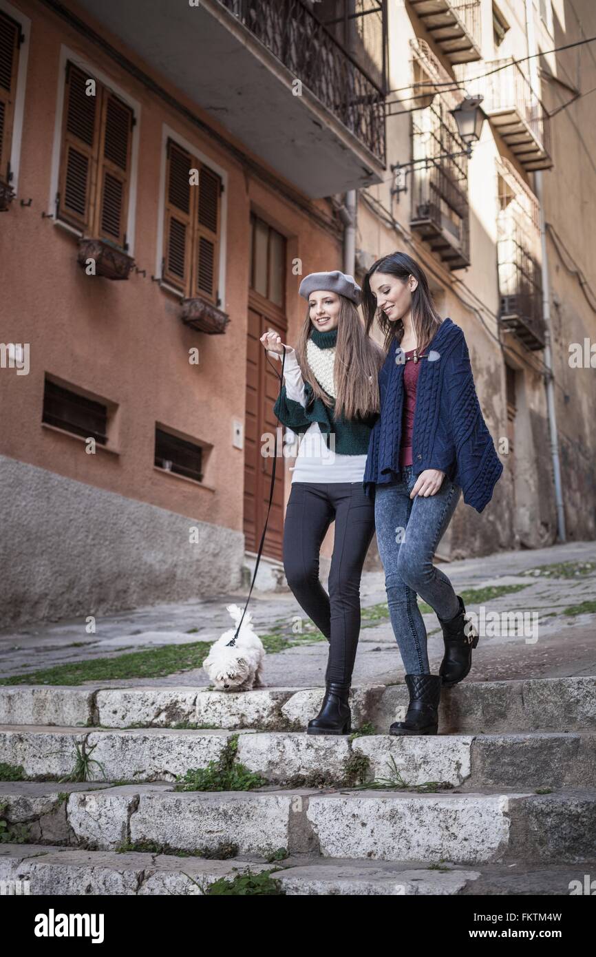 Low angle view   young women with dog walking down stone steps arms in arm smiling Stock Photo