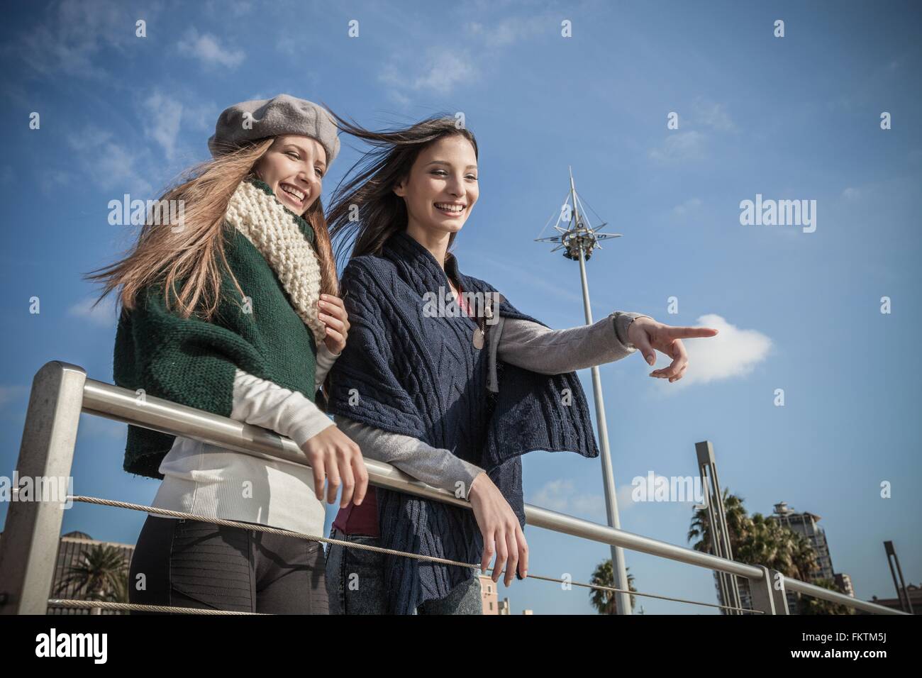 Low angle view   young women leaning against railing looking away pointing and smiling Stock Photo