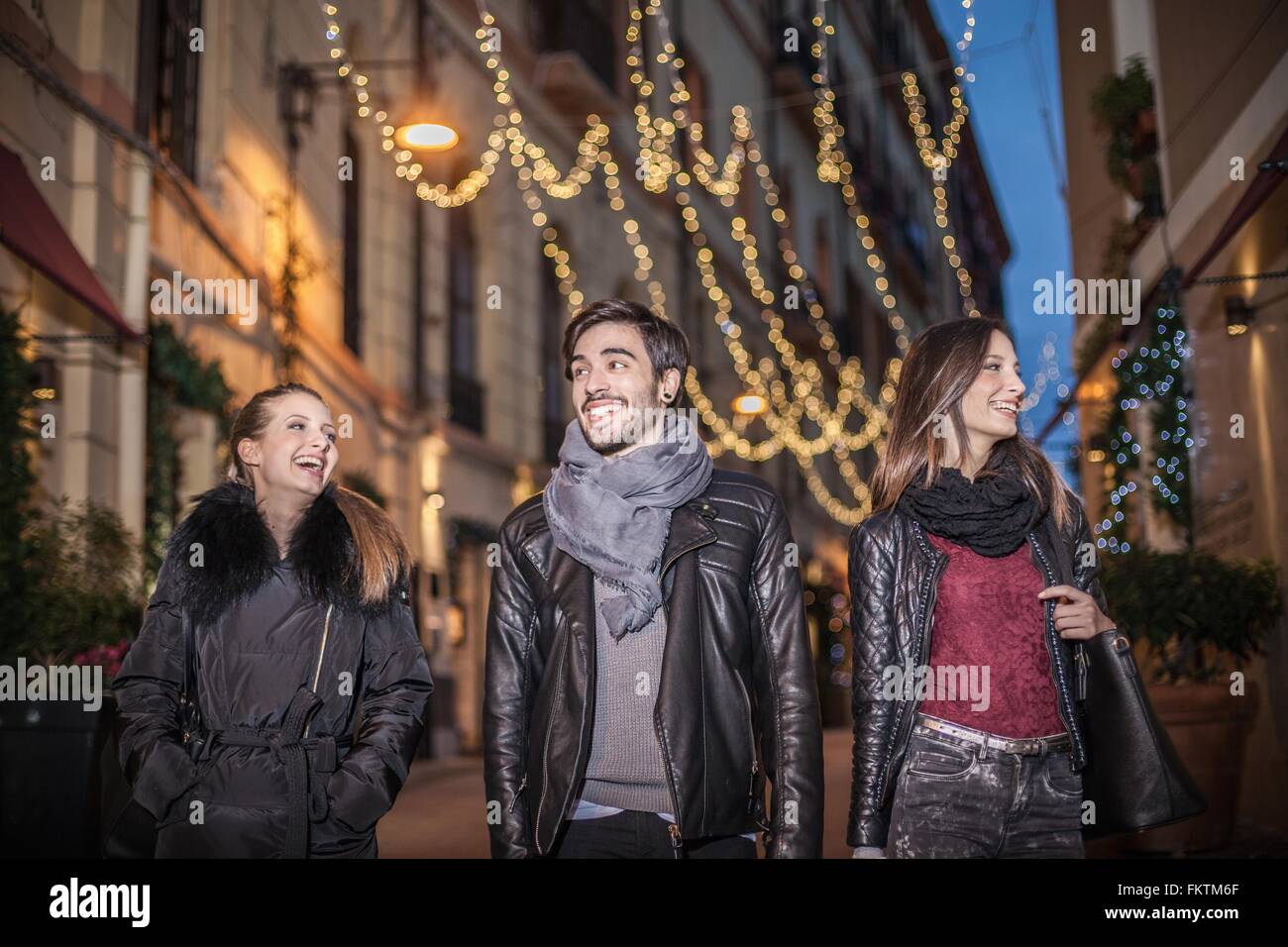 Low angle front view   friends walking down street in the evening smiling Stock Photo
