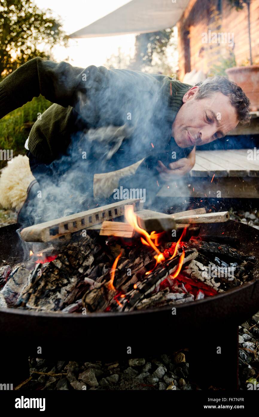 Mature man leaning to inspect fire pit Stock Photo