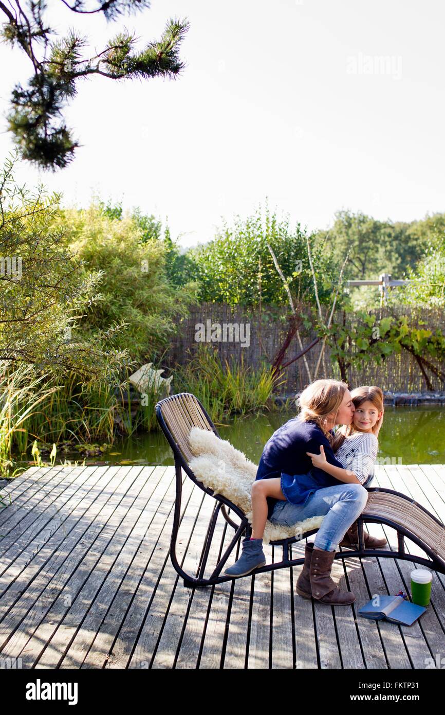 Mother and daughter hugging on lounge chair on decking Stock Photo