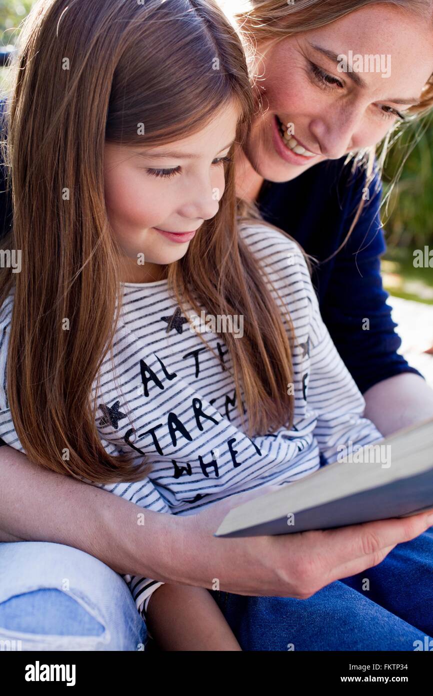 Mother and daughter reading book together, smiling Stock Photo