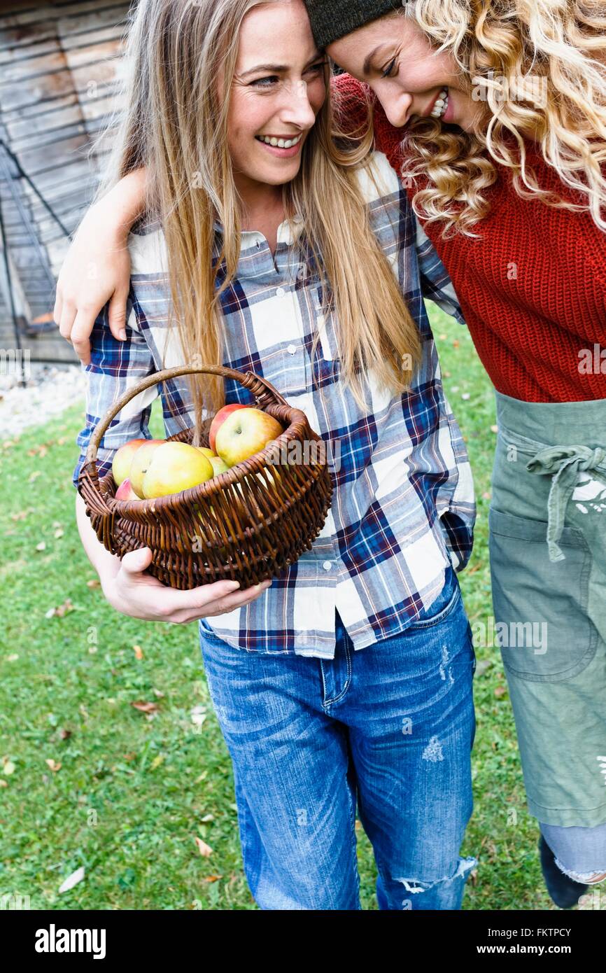 Two friends with arms round each other, one carrying basket   apples Stock Photo