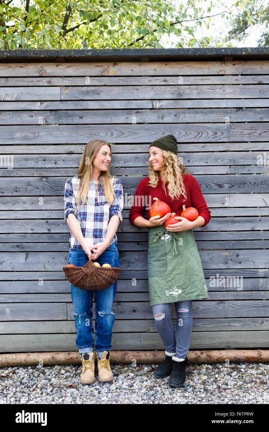 Two friends holding homegrown produce by wooden shed Stock Photo