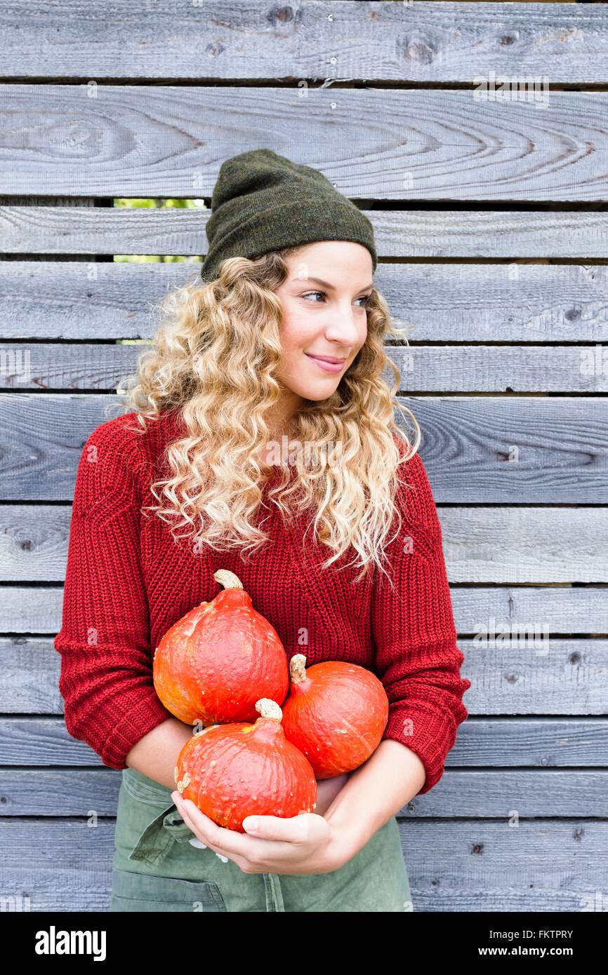 Young woman by wooden shed holding squash, looking away Stock Photo
