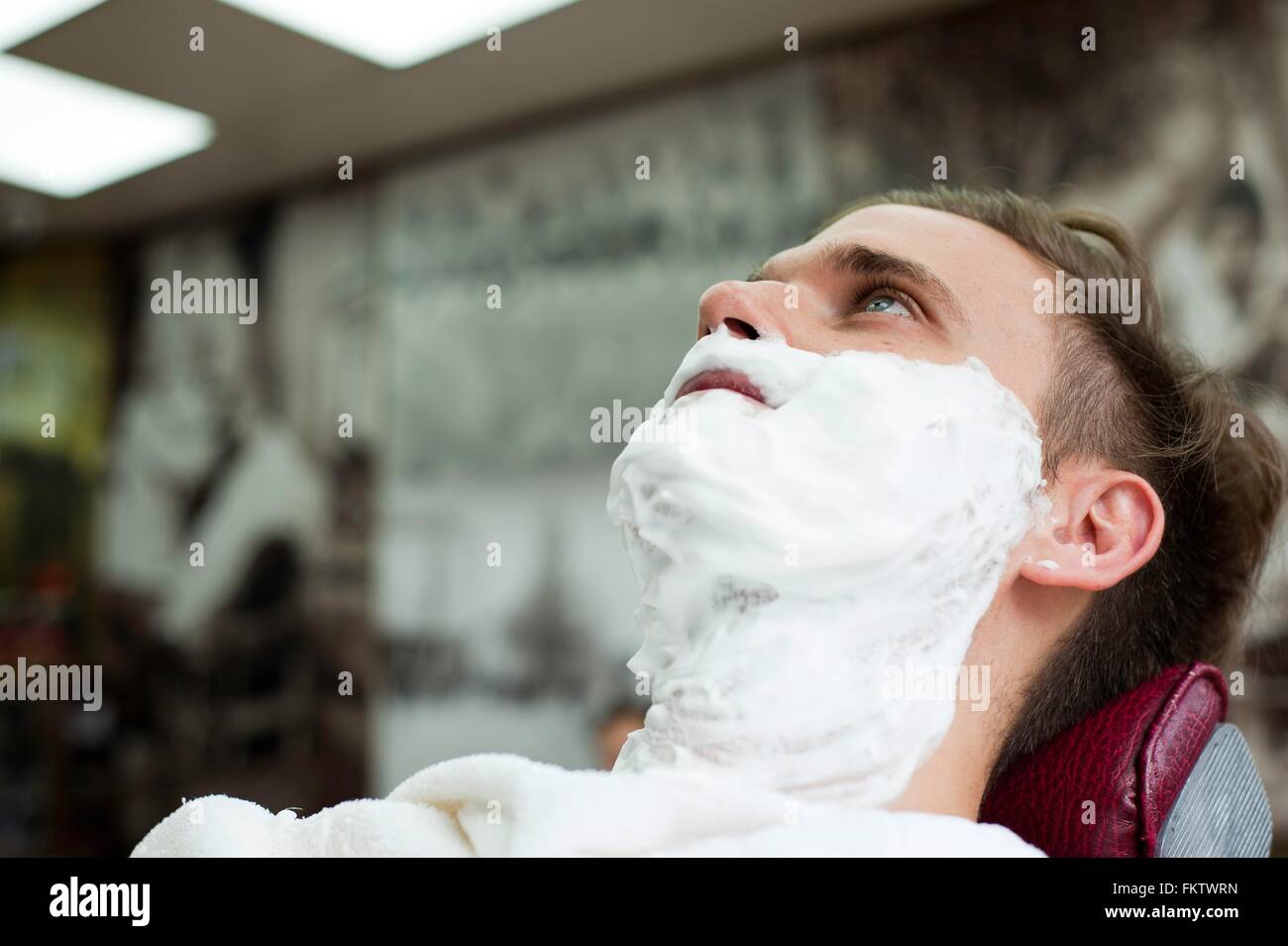 Young man in with face covered in shaving cream looking up