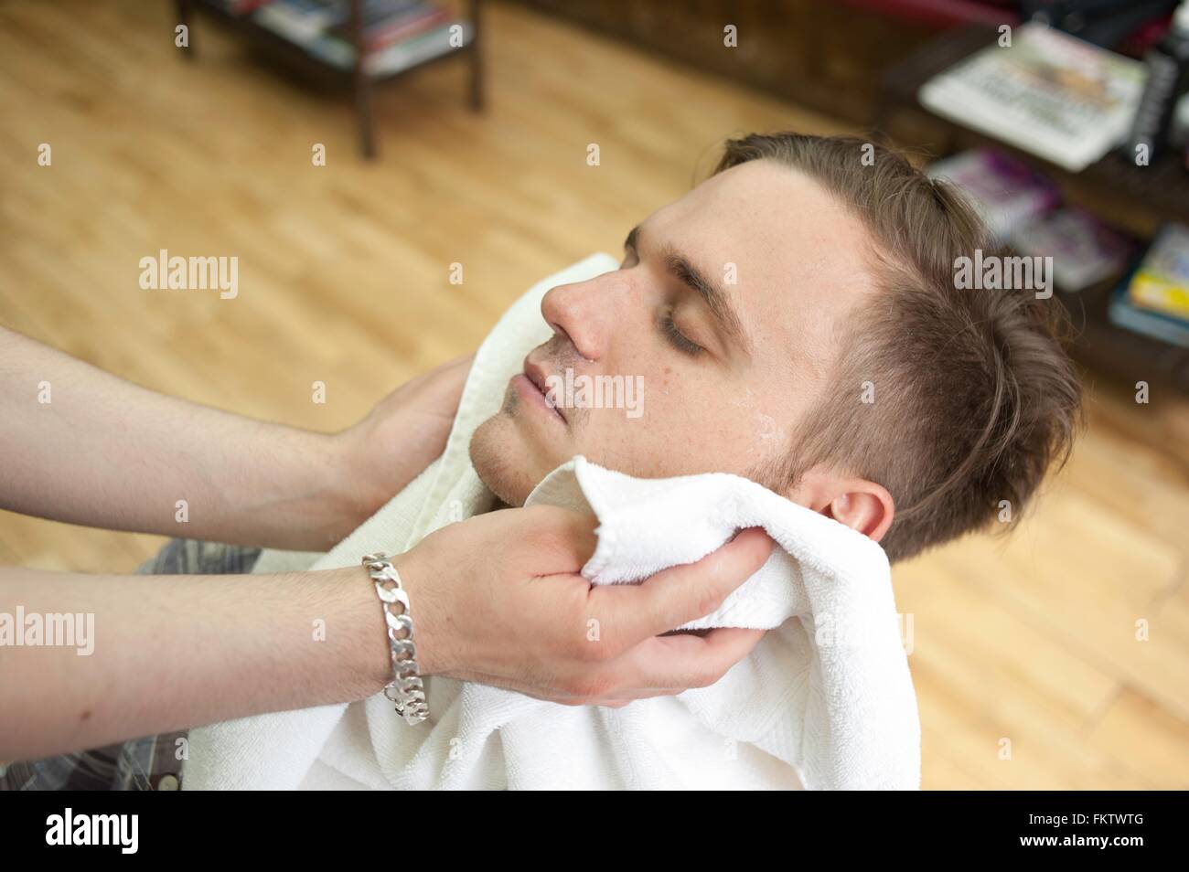 High angle side view of young man in barbershop, head back, eyes closed having face dried with towel Stock Photo