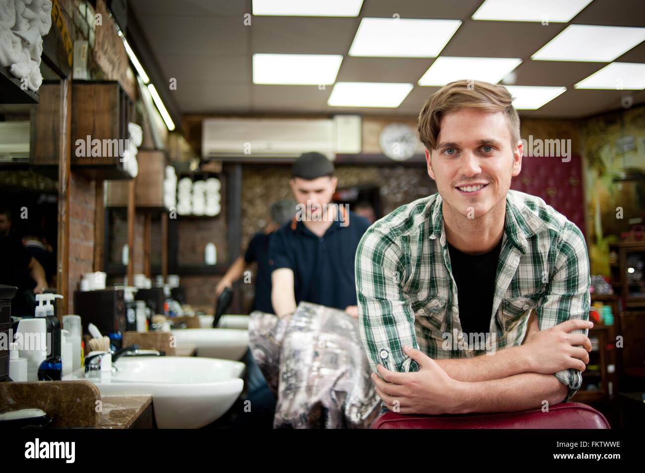 Young man in barbershop resting on elbows looking at camera smiling Stock Photo