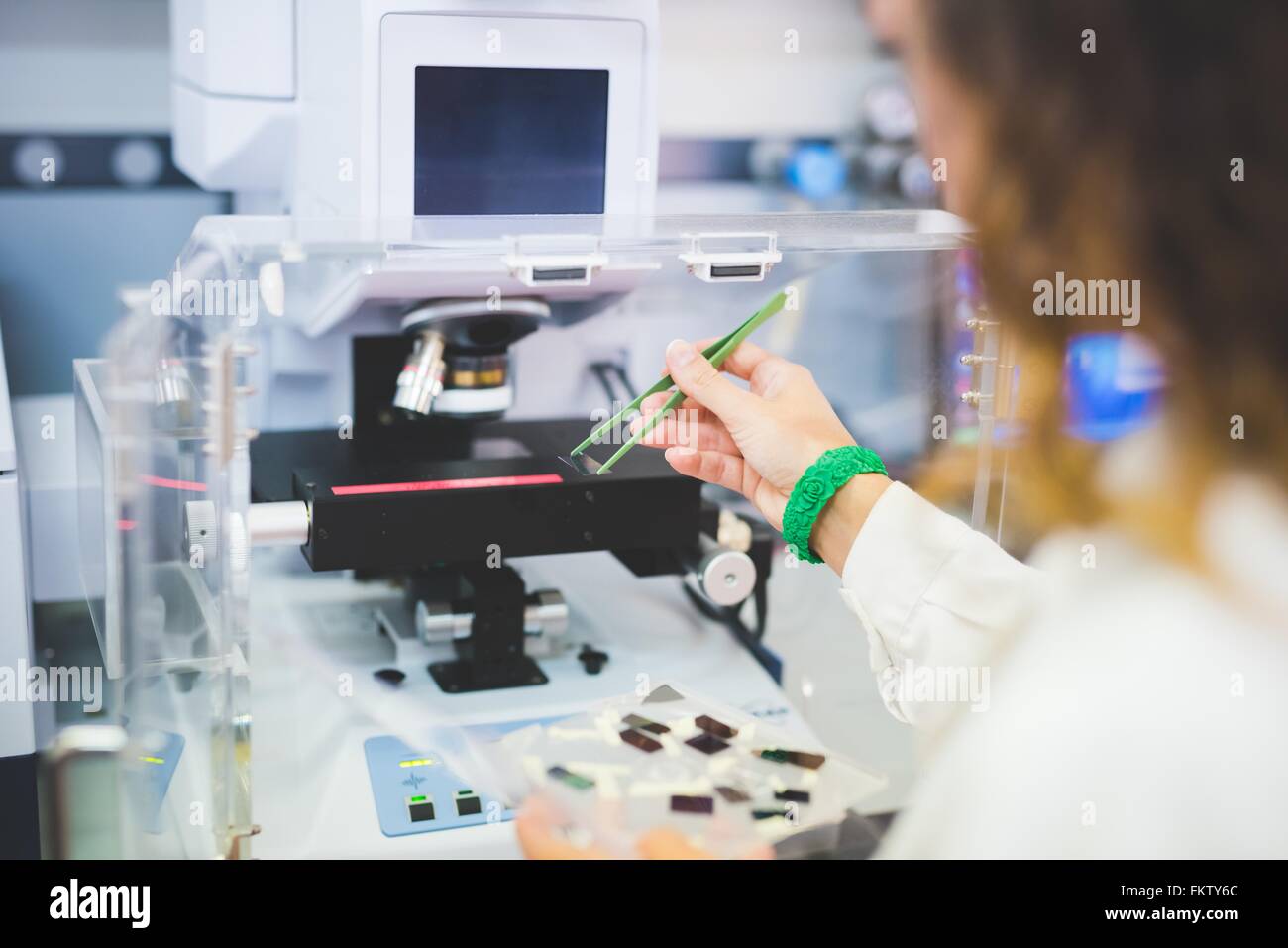 Female scientist using FTIR spectrophotometer, positioning thin film sample on microscope stage Stock Photo