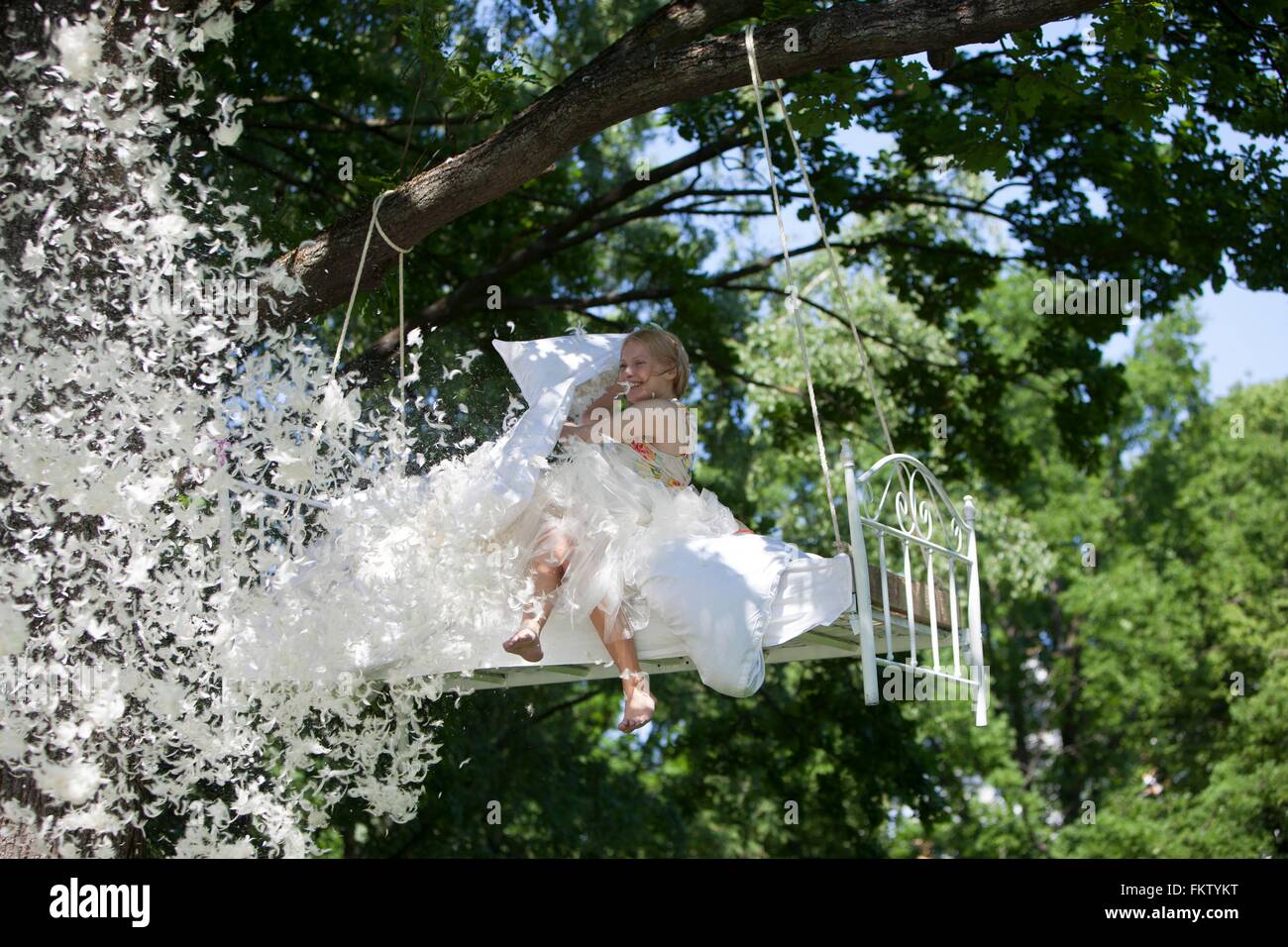 Young woman sitting on bed, emptying feathers from pillow, bed hanging