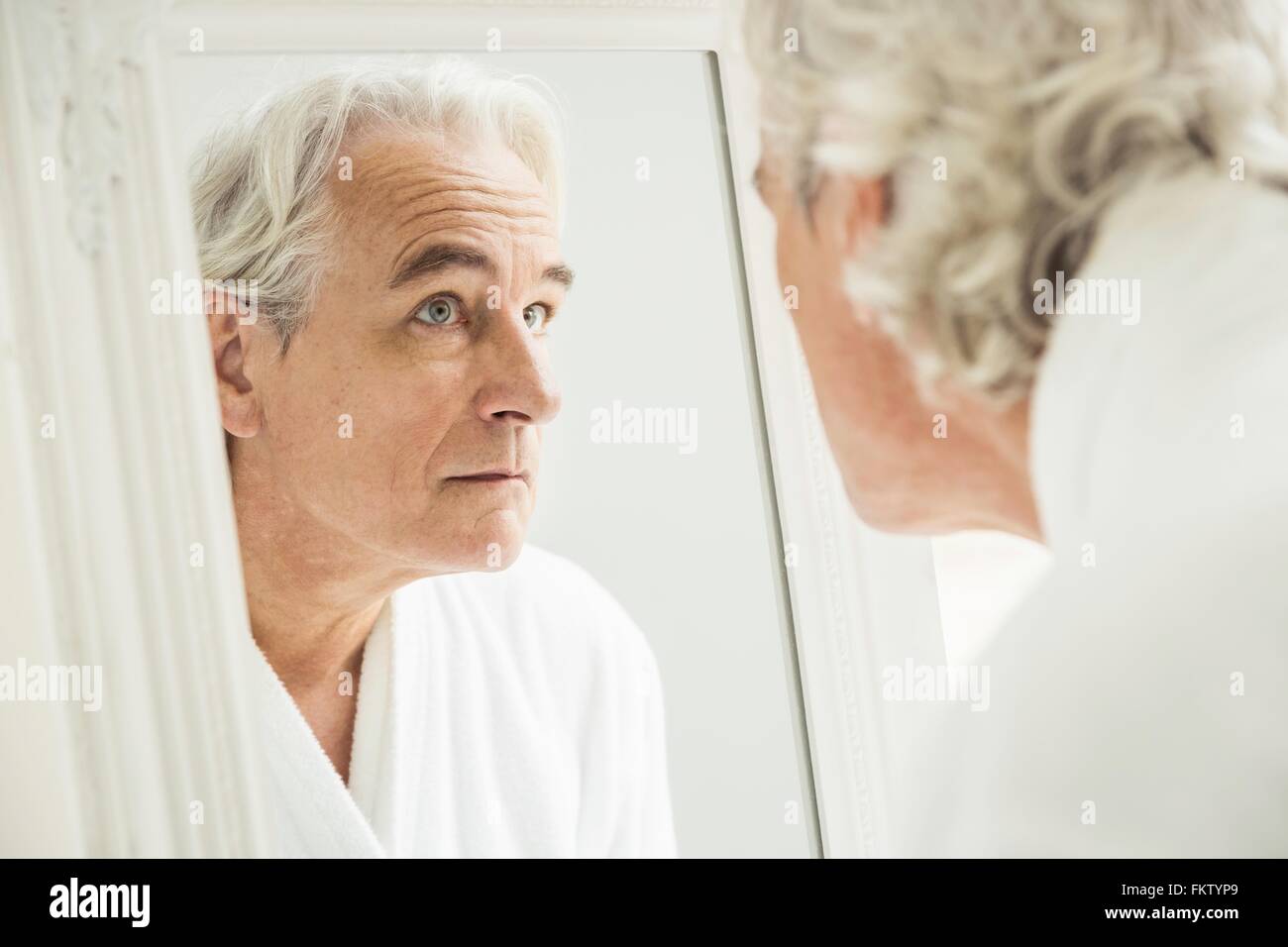Grey haired senior man staring at himself in mirror Stock Photo