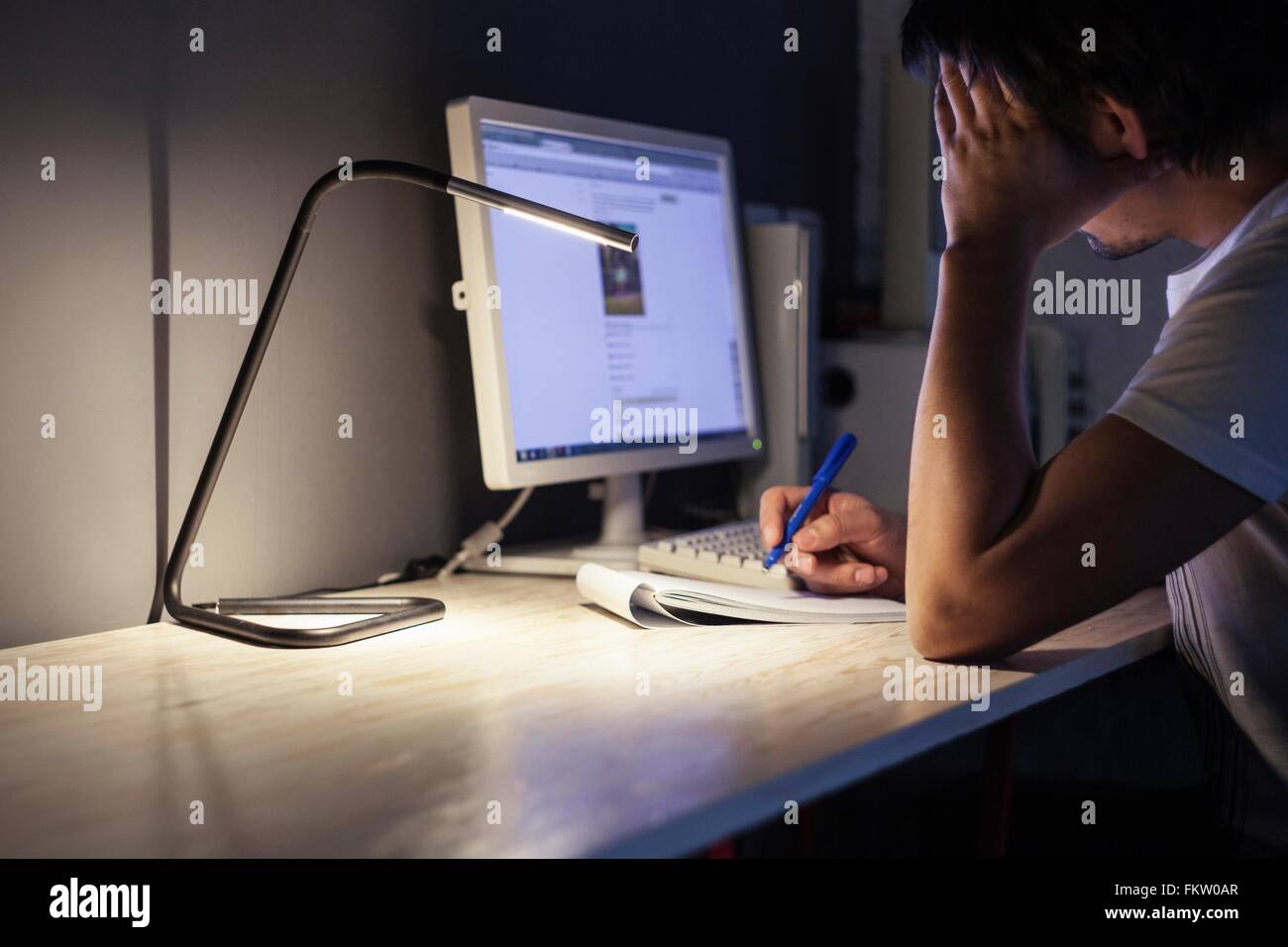 Tired man using desktop computer and making notes Stock Photo