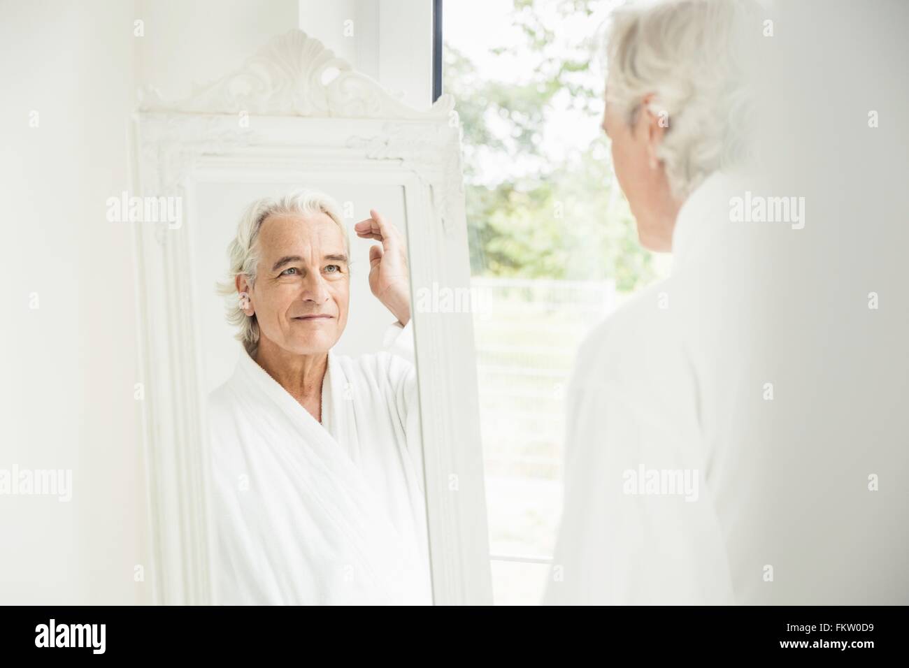 Happy grey haired senior man wearing bathrobe looking at himself in mirror Stock Photo