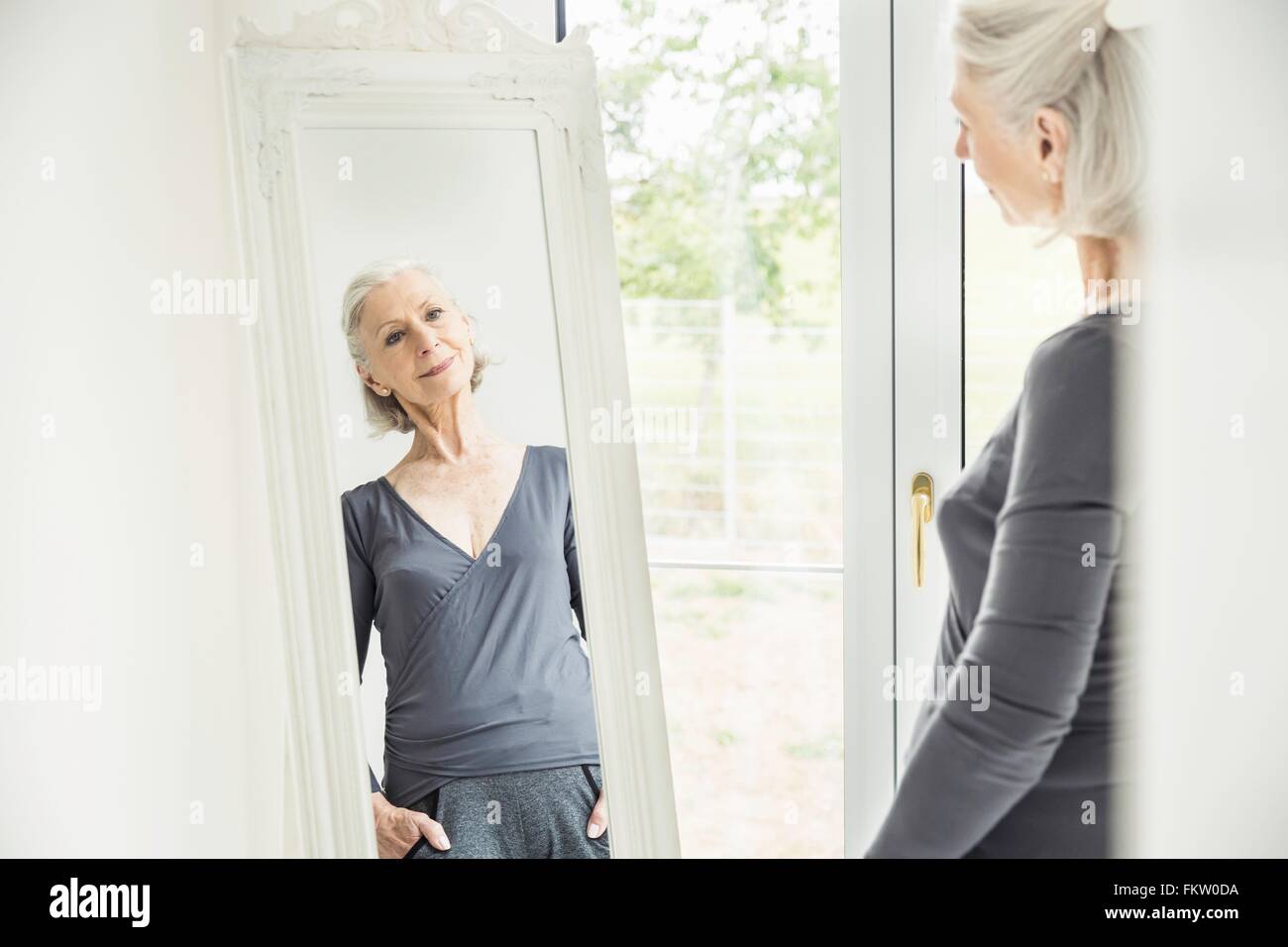 Grey haired senior woman admiring herself in mirror Stock Photo