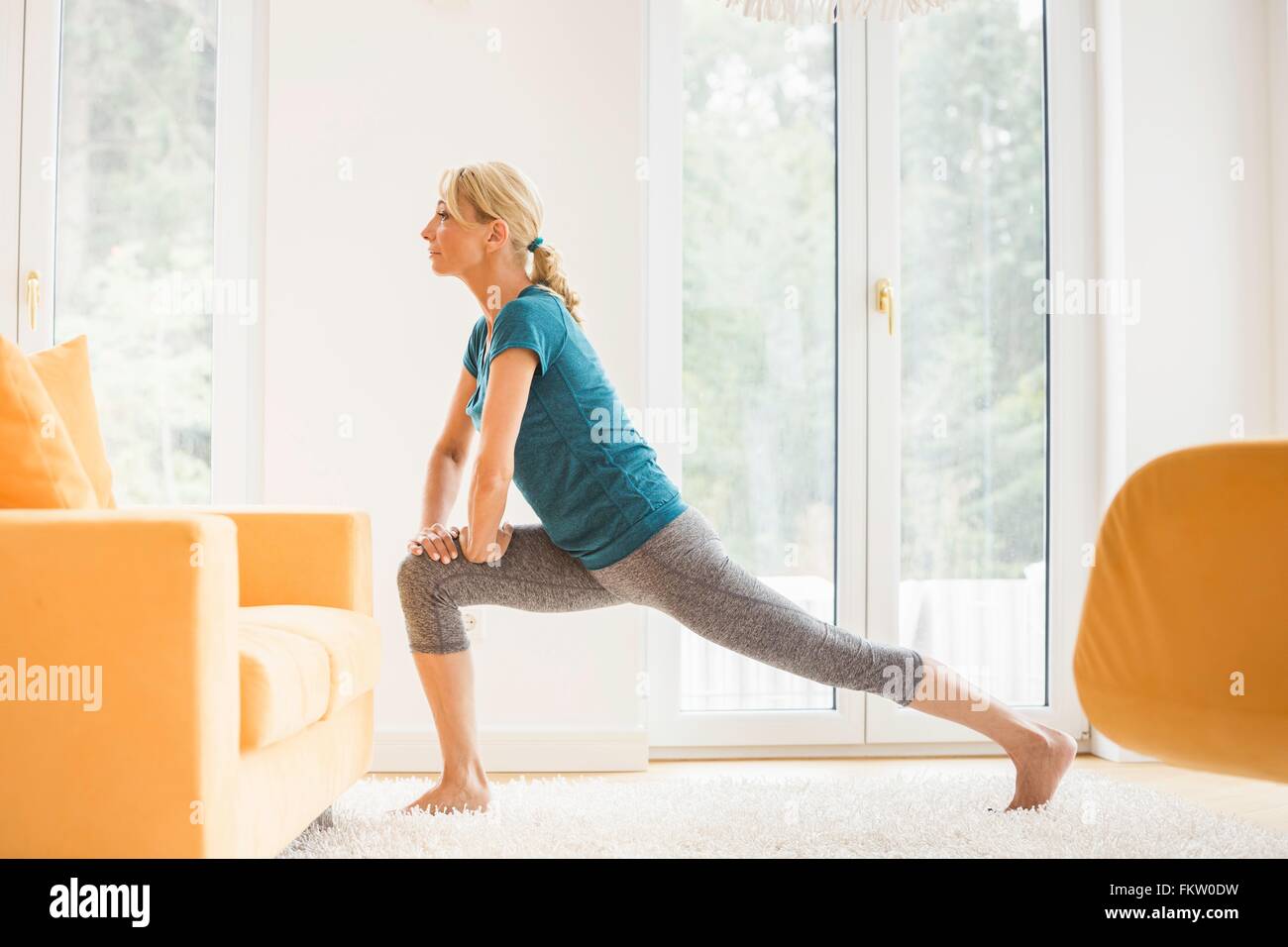 Mature woman doing lunge stretch exercise in living room Stock Photo