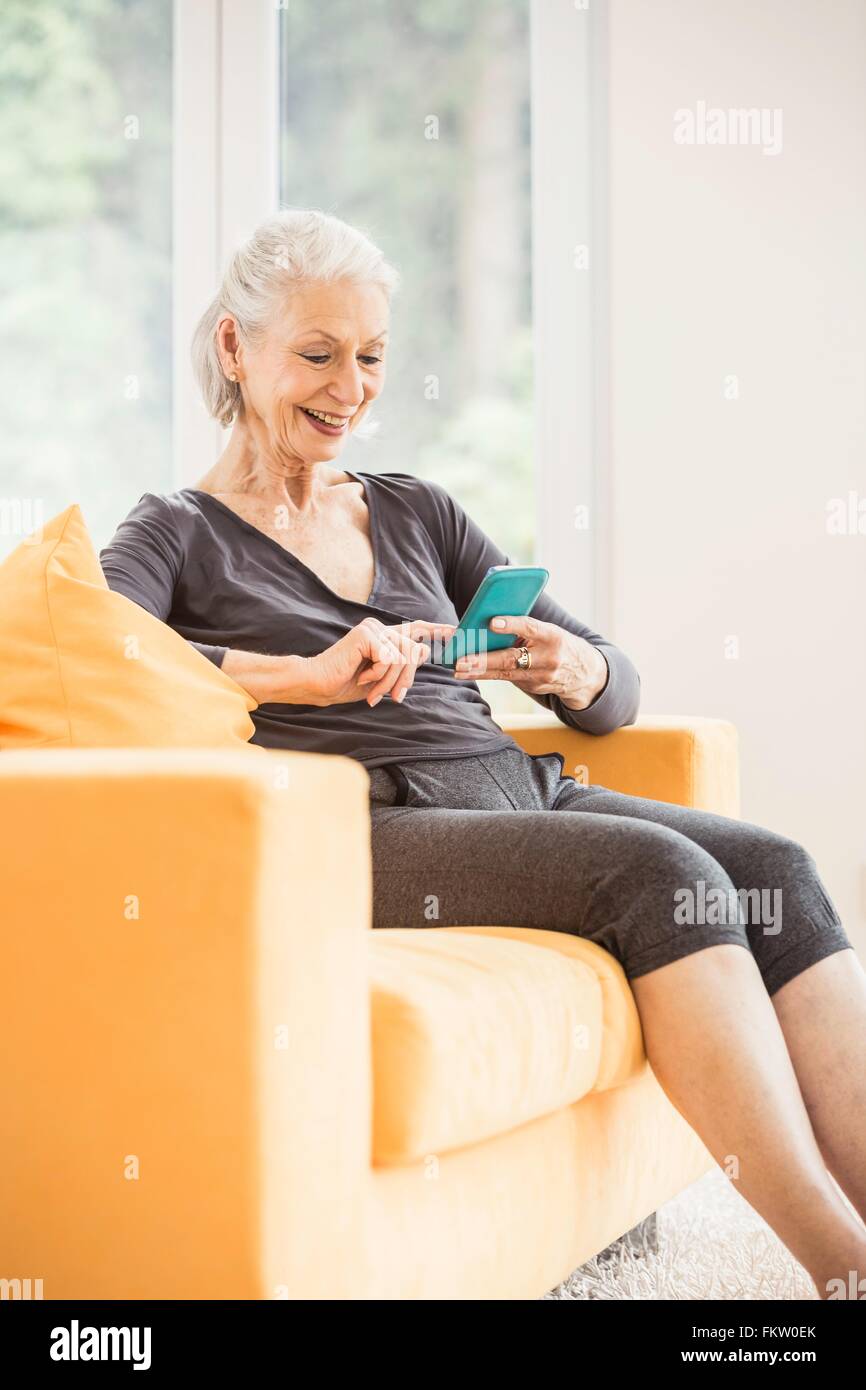 Senior woman taking a break from exercising using smartphone on living room sofa Stock Photo
