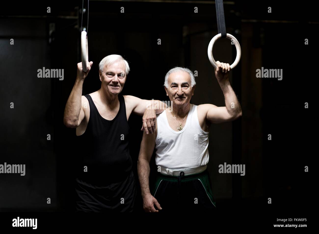 Portrait of two senior men holding gym rings in dark gym Stock Photo